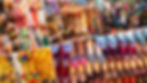 Vibrant  New Delhi flee market scene with colorful fabrics, embroidered shoes, and handmade bags. Shoppers browse under a patterned canopy with lights.